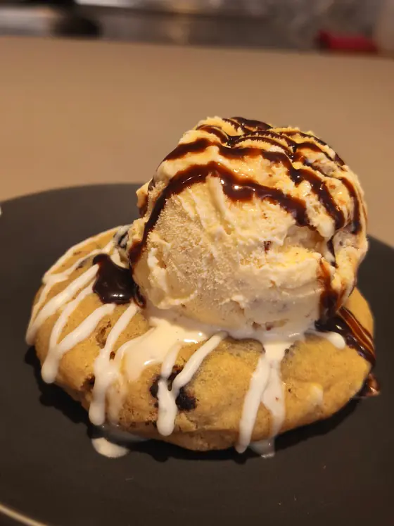 Cookie tibia coronada con una bocha de helado y sirope de chocolate