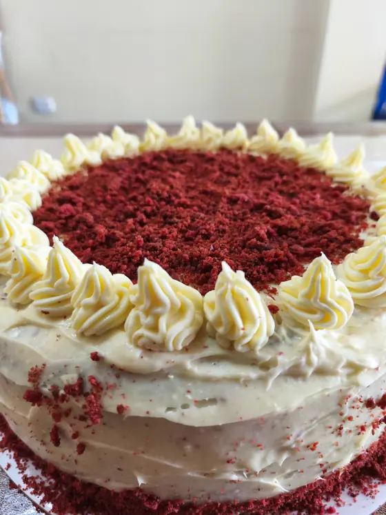 Torta red velvet cubierta con frosting de queso crema y rosetas alrededor del borde