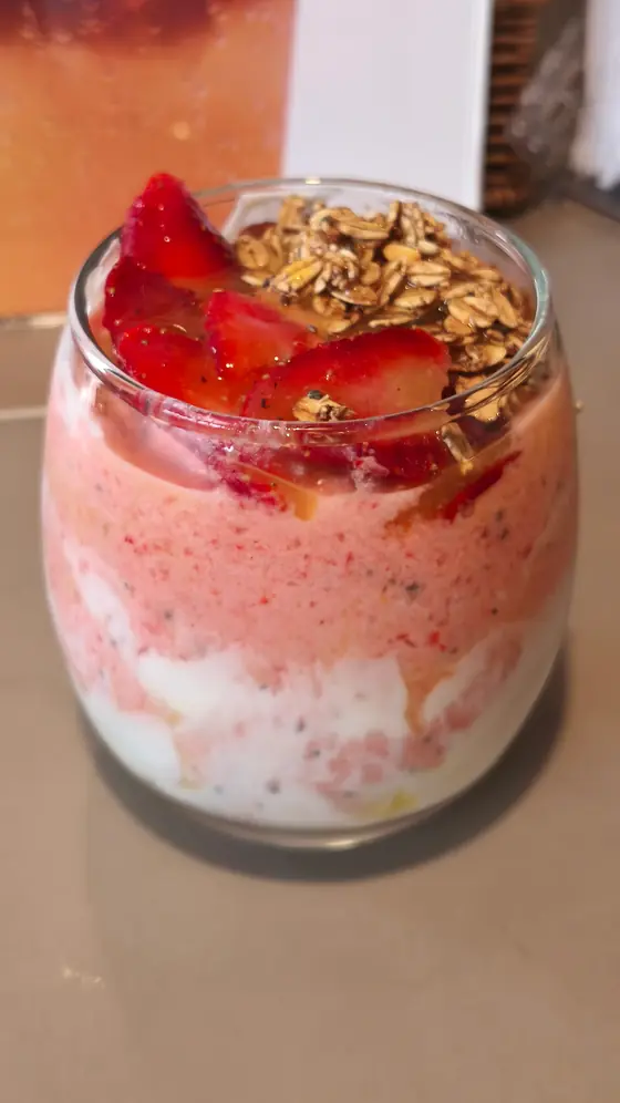Vaso de yogurt con fresas frescas y granola encima